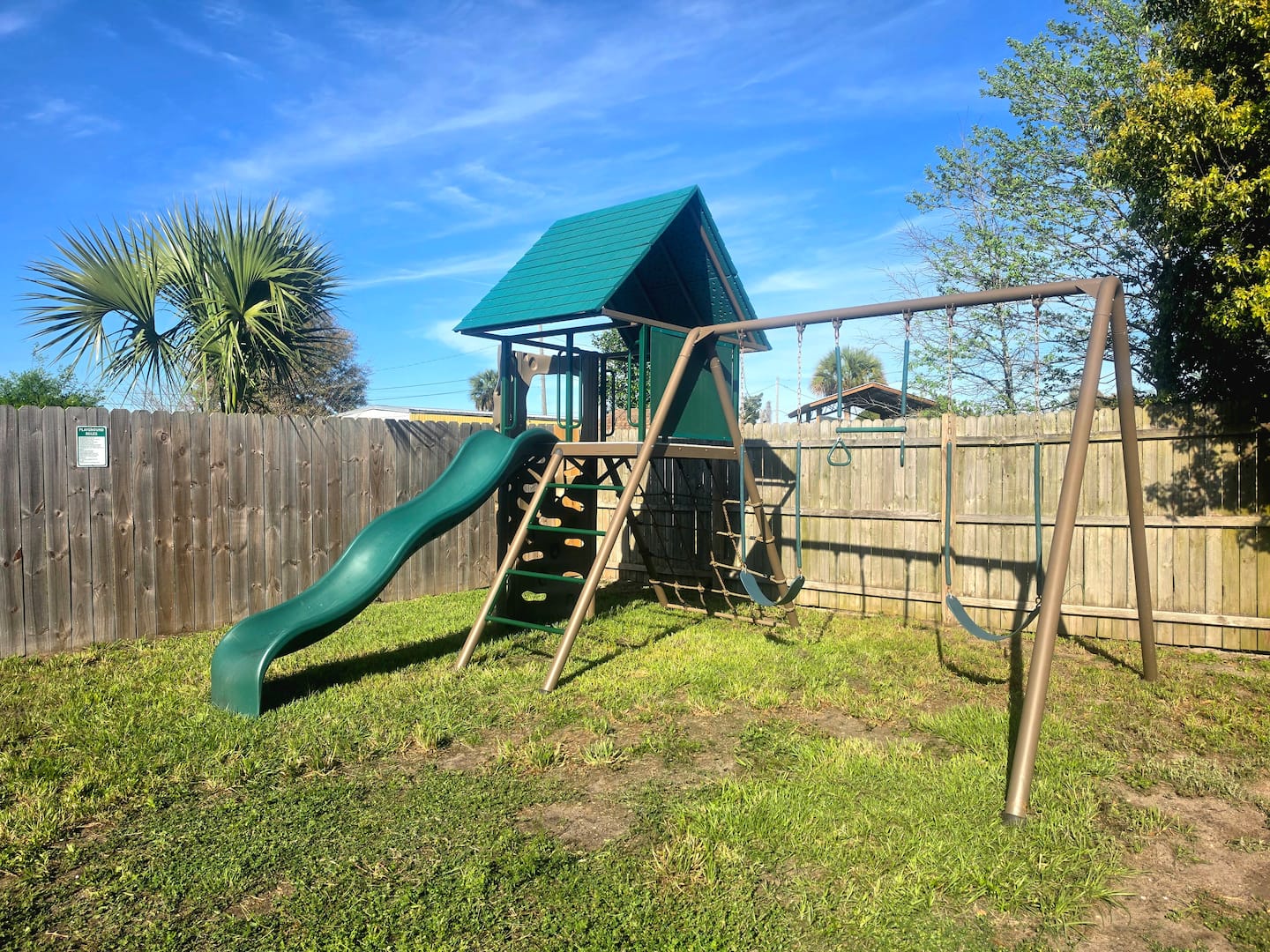 Backyard playset with slide, climbing wall, and swings inside the fenced yard.
